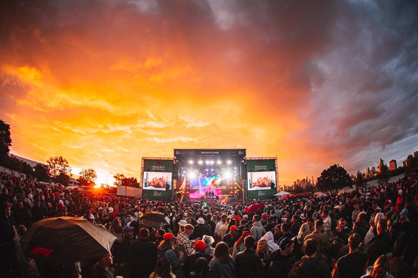 Crowd watching a band perform on the Main Stage at the Australian Grand Prix under a dramatic orange sunset sky