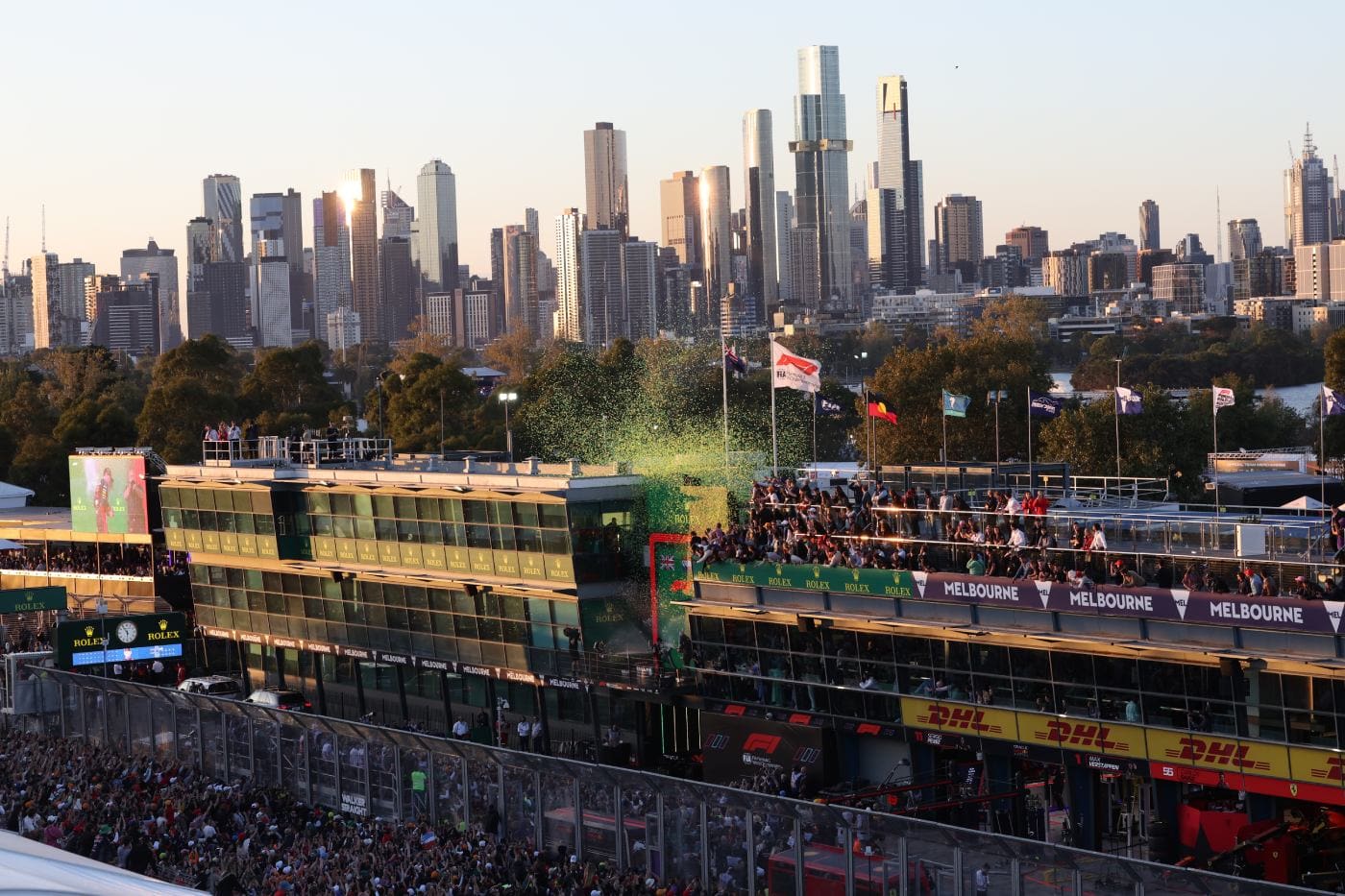 Melbourne city skyline behind the pit building and podium at the Australian Grand Prix, with fans celebrating on the podium terrace